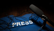 Media Journalism Global Daily News Content Concept. Blue journalist (press) vest in dark with backlight and fog. Media microphone on journalist vest. Selective focus