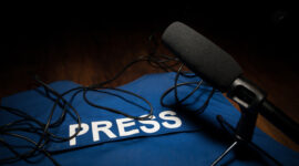 Media Journalism Global Daily News Content Concept. Blue journalist (press) vest in dark with backlight and fog. Media microphone on journalist vest. Selective focus